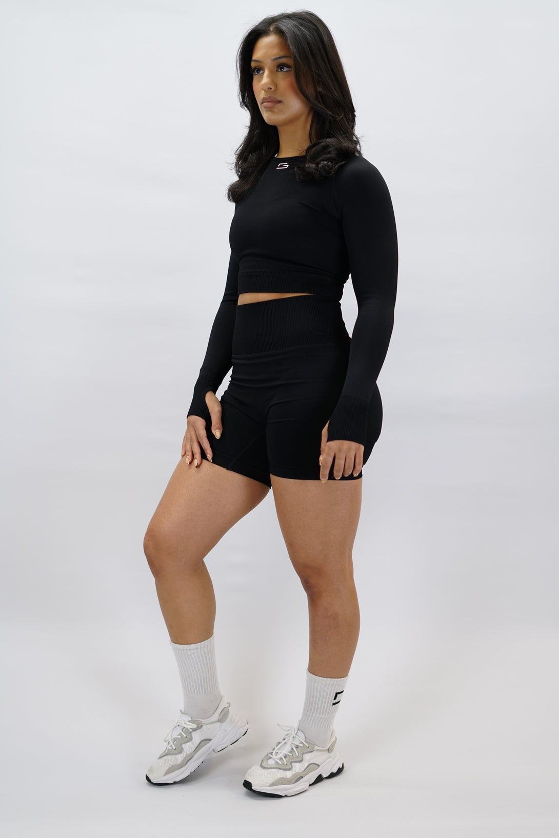 Svart Celia Long-Sleeve Crop Top, en cropped långärmad träningströja med G-symbol på framsidan och Gymwear-logotyp baktill
