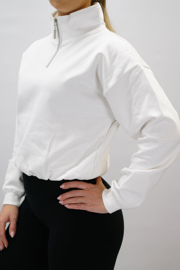 Vit Delia Half-Zip Long Sleeve, en långärmad tröja i 100% bomull med halvdragkedja vid halsen och diskret ton-i-ton Gymwear-logotyp centrerat på bröstet.