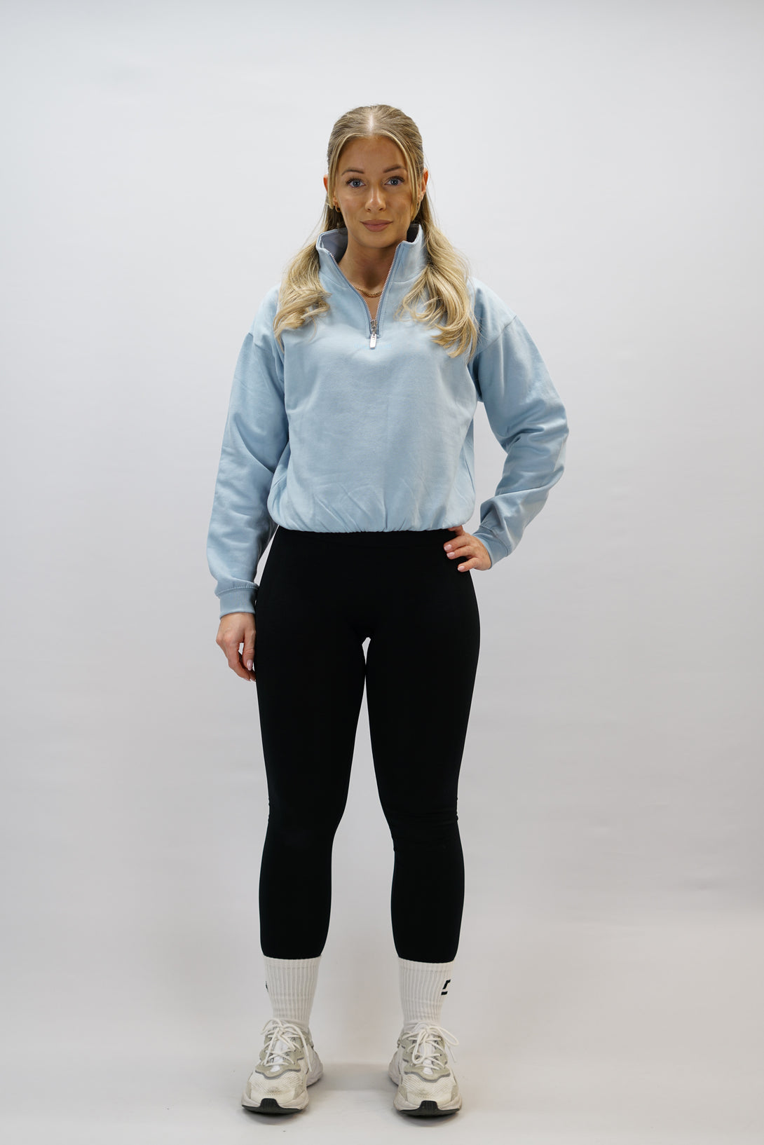 Blå Delia Half-Zip Long Sleeve, en långärmad tröja i 100% bomull med halvdragkedja vid halsen och diskret ton-i-ton Gymwear-logotyp centrerat på bröstet.