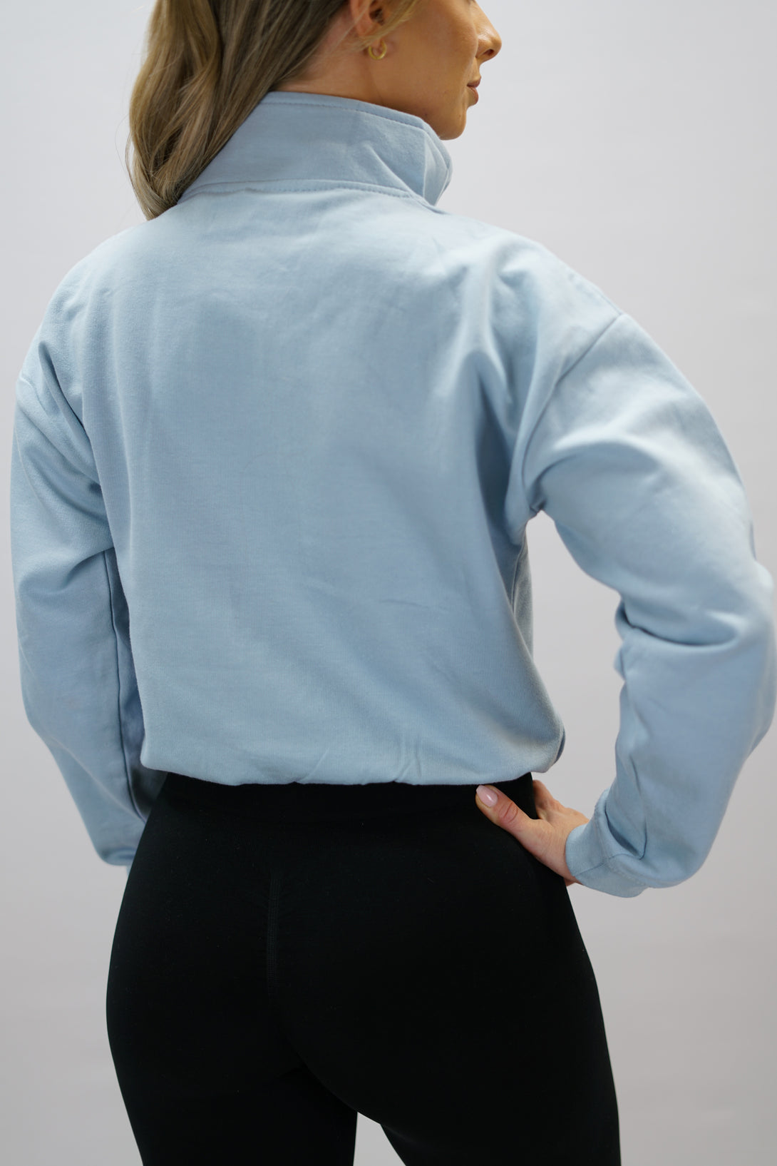 Blå Delia Half-Zip Long Sleeve, en långärmad tröja i 100% bomull med halvdragkedja vid halsen och diskret ton-i-ton Gymwear-logotyp centrerat på bröstet.