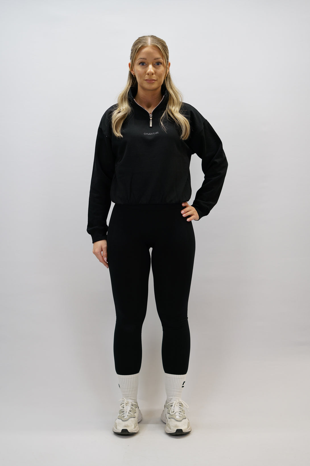 Svart Delia Half-Zip Long Sleeve, en långärmad tröja i 100% bomull med halvdragkedja vid halsen och diskret ton-i-ton Gymwear-logotyp centrerat på bröstet.