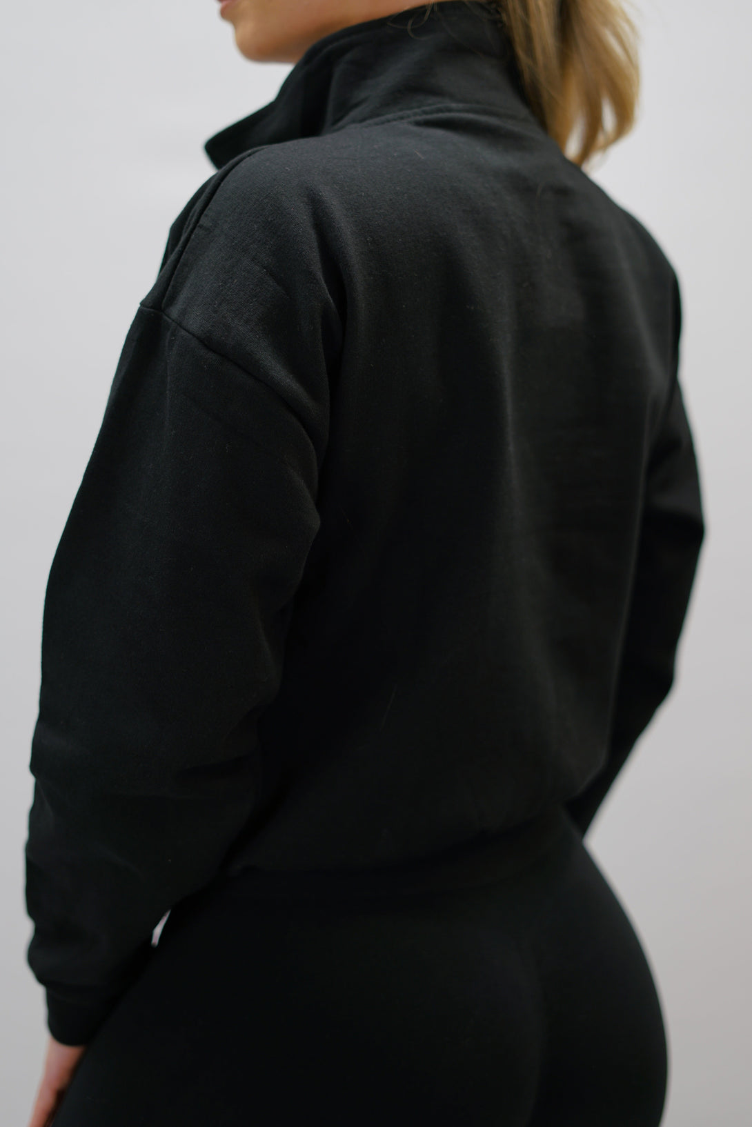 Svart Delia Half-Zip Long Sleeve, en långärmad tröja i 100% bomull med halvdragkedja vid halsen och diskret ton-i-ton Gymwear-logotyp centrerat på bröstet.