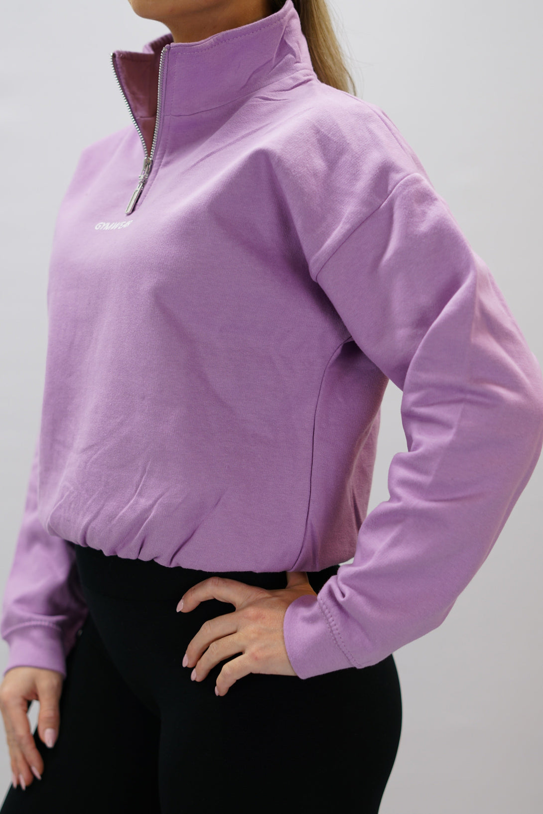 Lila Delia Half-Zip Long Sleeve, en långärmad tröja i 100% bomull med halvdragkedja vid halsen och diskret ton-i-ton Gymwear-logotyp centrerat på bröstet.