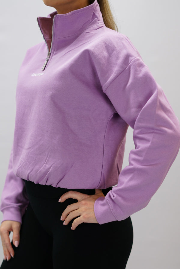 Lila Delia Half-Zip Long Sleeve, en långärmad tröja i 100% bomull med halvdragkedja vid halsen och diskret ton-i-ton Gymwear-logotyp centrerat på bröstet.