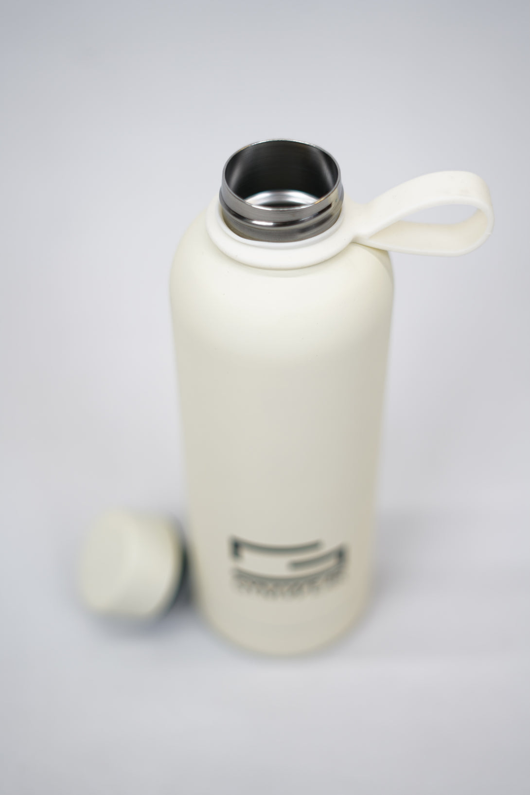 GYMWEAR Bottle 500ml, en beige rostfri vattenflaska med silikon beläggning, kapacitet 500 milliliter, med tryckt Gymwear-logotyp och symbol