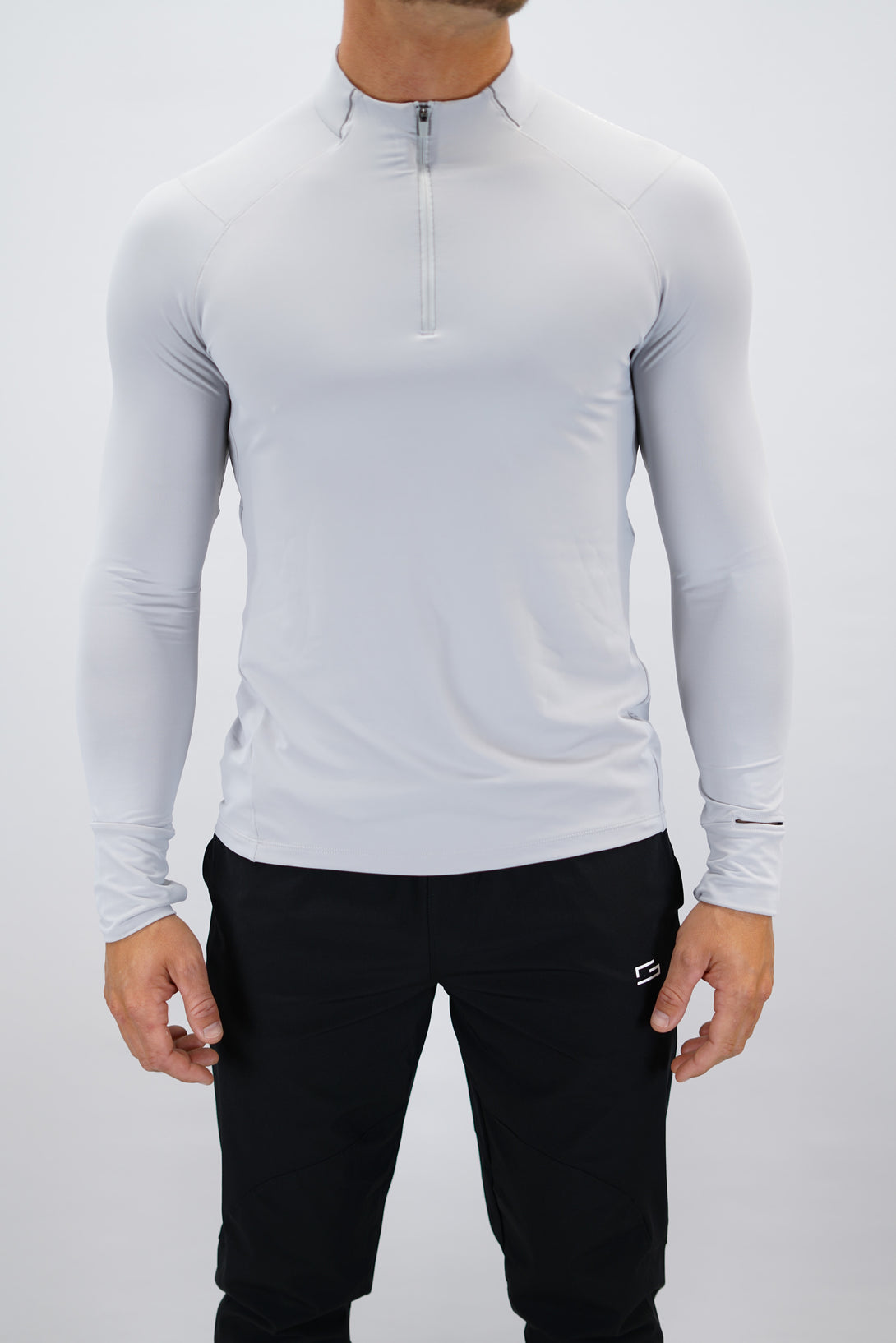 Ljusgrå Zayne Half-Zip Long Sleeve – Reflective Detail - långärmad träningströja med halvdragkedja, tumhål, klockutrymme, reflekterande detalj vid kragen och Gymwear-logga på framsidan