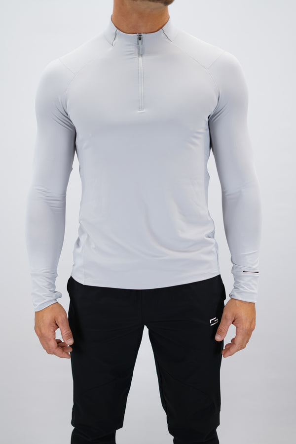 Ljusgrå Zayne Half-Zip Long Sleeve – Reflective Detail - långärmad träningströja med halvdragkedja, tumhål, klockutrymme, reflekterande detalj vid kragen och Gymwear-logga på framsidan