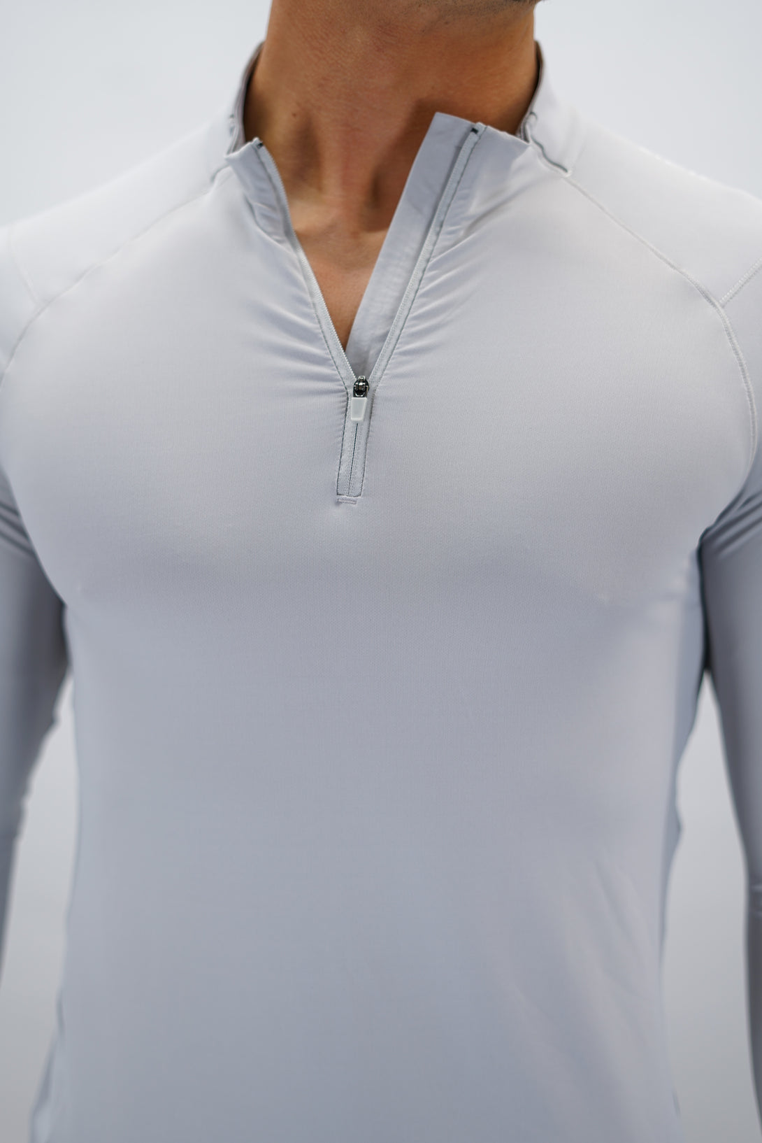 Ljusgrå Zayne Half-Zip Long Sleeve – Reflective Detail - långärmad träningströja med halvdragkedja, tumhål, klockutrymme, reflekterande detalj vid kragen och Gymwear-logga på framsidan