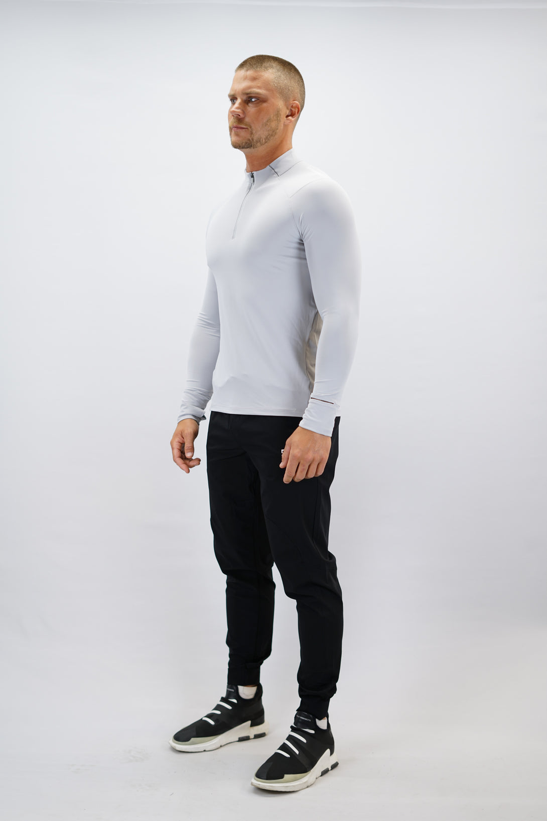 Ljusgrå Zayne Half-Zip Long Sleeve – Reflective Detail - långärmad träningströja med halvdragkedja, tumhål, klockutrymme, reflekterande detalj vid kragen och Gymwear-logga på framsidan