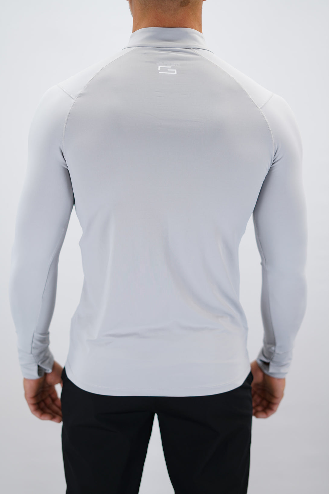 Ljusgrå Zayne Half-Zip Long Sleeve – Reflective Detail - långärmad träningströja med halvdragkedja, tumhål, klockutrymme, reflekterande detalj vid kragen och Gymwear-logga på framsidan