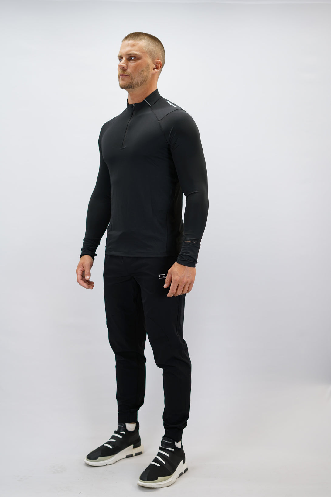 Svart Zayne Half-Zip Long Sleeve – Reflective Detail - långärmad träningströja med halvdragkedja, tumhål, klockutrymme, reflekterande detalj vid kragen och Gymwear-logga på framsidan