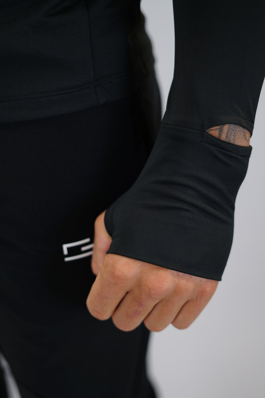 Svart Zayne Half-Zip Long Sleeve – Reflective Detail - långärmad träningströja med halvdragkedja, tumhål, klockutrymme, reflekterande detalj vid kragen och Gymwear-logga på framsidan