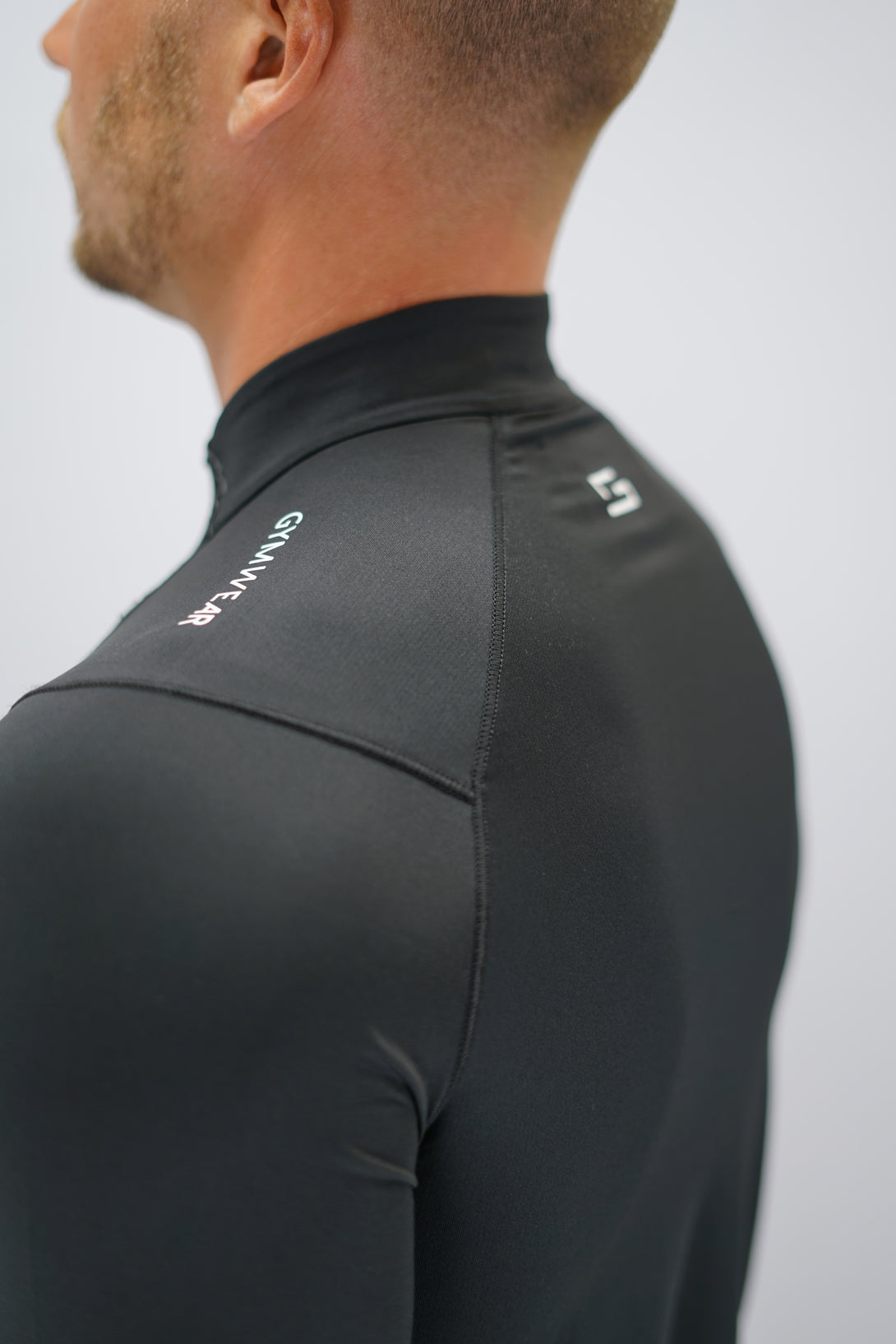 Svart Zayne Half-Zip Long Sleeve – Reflective Detail - långärmad träningströja med halvdragkedja, tumhål, klockutrymme, reflekterande detalj vid kragen och Gymwear-logga på framsidan