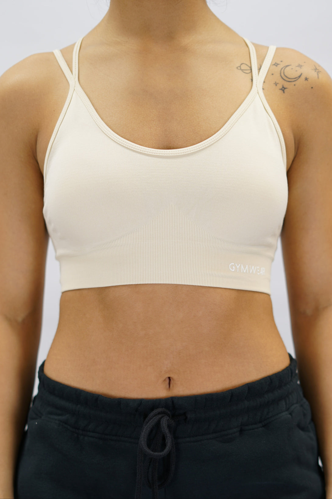 Beige Eily Cross Bra - sport-bh med korsade axelband baktill och Gymwear-logga på vänster nedre kant