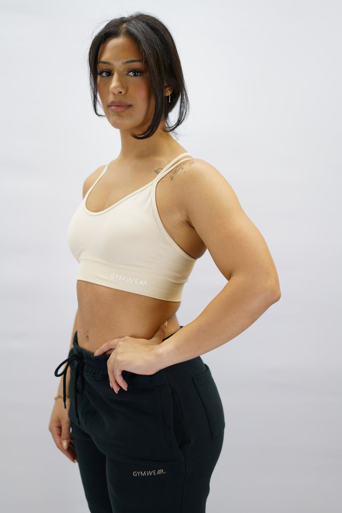 Beige Eily Cross Bra - sport-bh med korsade axelband baktill och Gymwear-logga på vänster nedre kant