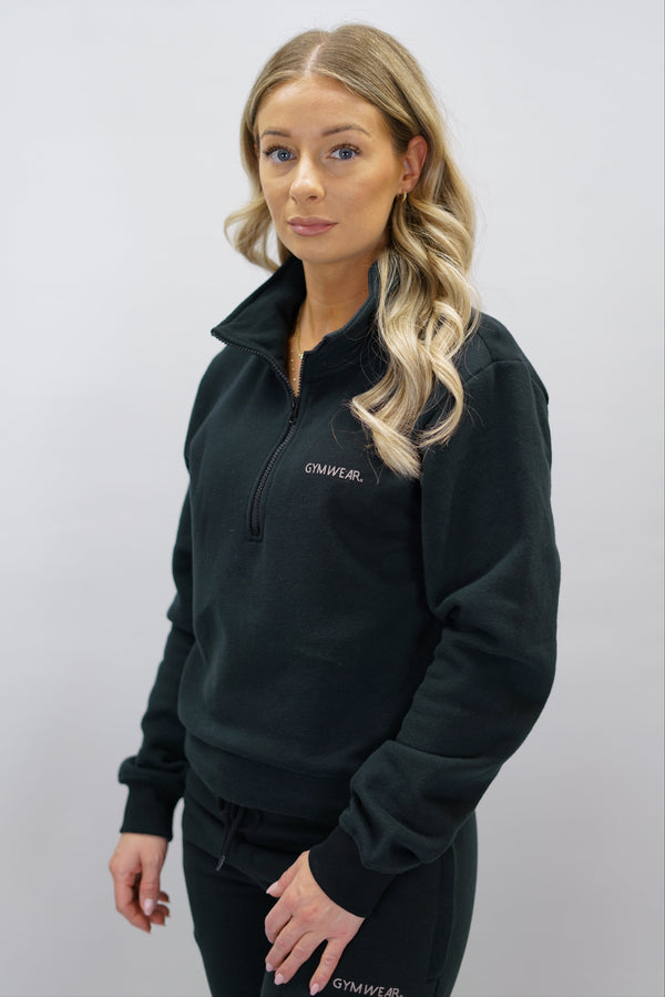 Half-Zip Sweater för dam i mjuk borstad bomull, svart färg, med logga på vänster bröst och symbol i nacken. Stilren och funktionell tröja för vardag och aktivitet.
