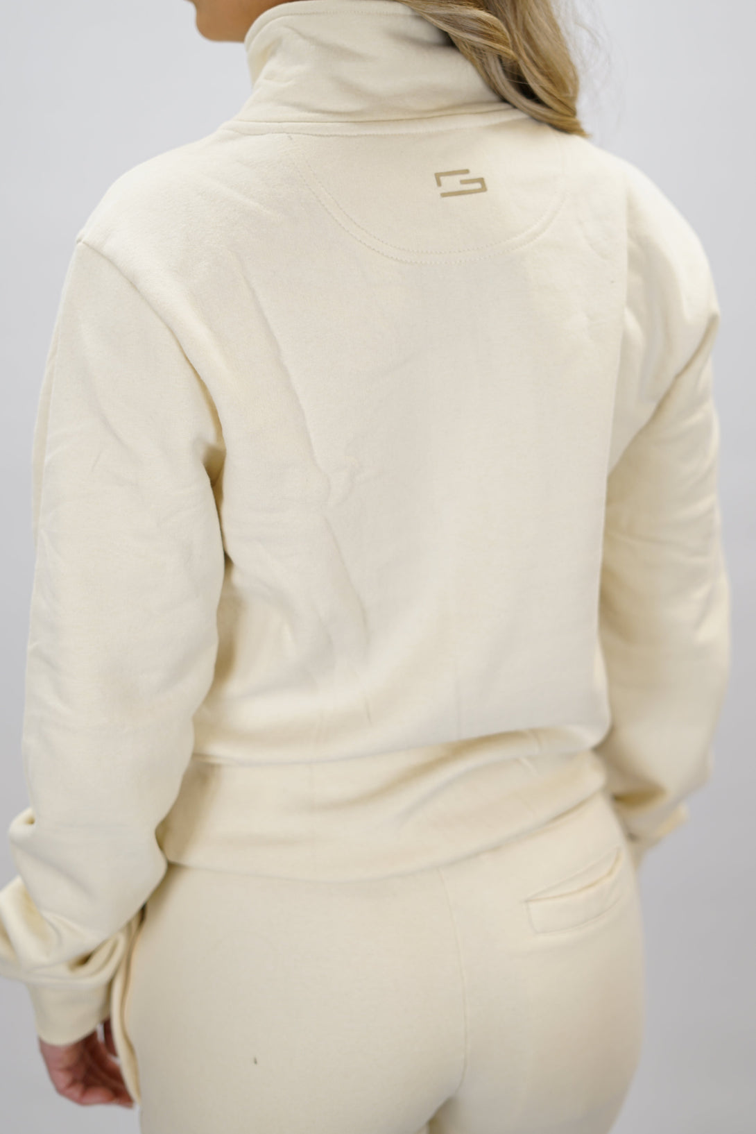 Half-Zip Sweater för dam i mjuk borstad bomull, beige färg, med logga på vänster bröst och symbol i nacken. Stilren och funktionell tröja för vardag och aktivitet.