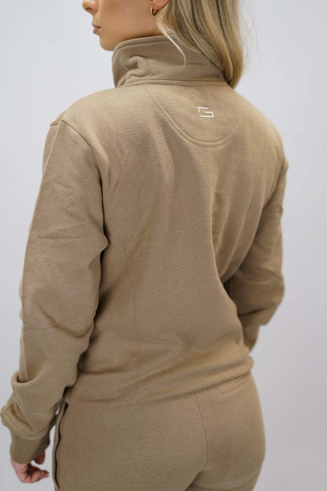 Half-Zip Sweater för dam i mjuk borstad bomull, brun färg, med logga på vänster bröst och symbol i nacken. Stilren och funktionell tröja för vardag och aktivitet.