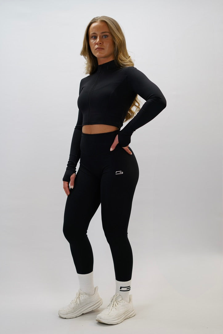 Svart Zoe Cropped Zip-up Top - cropped långärmad tröja med dragkedja, tumhål, Gymwear-logga på vänster axel och G-symbol i nacken