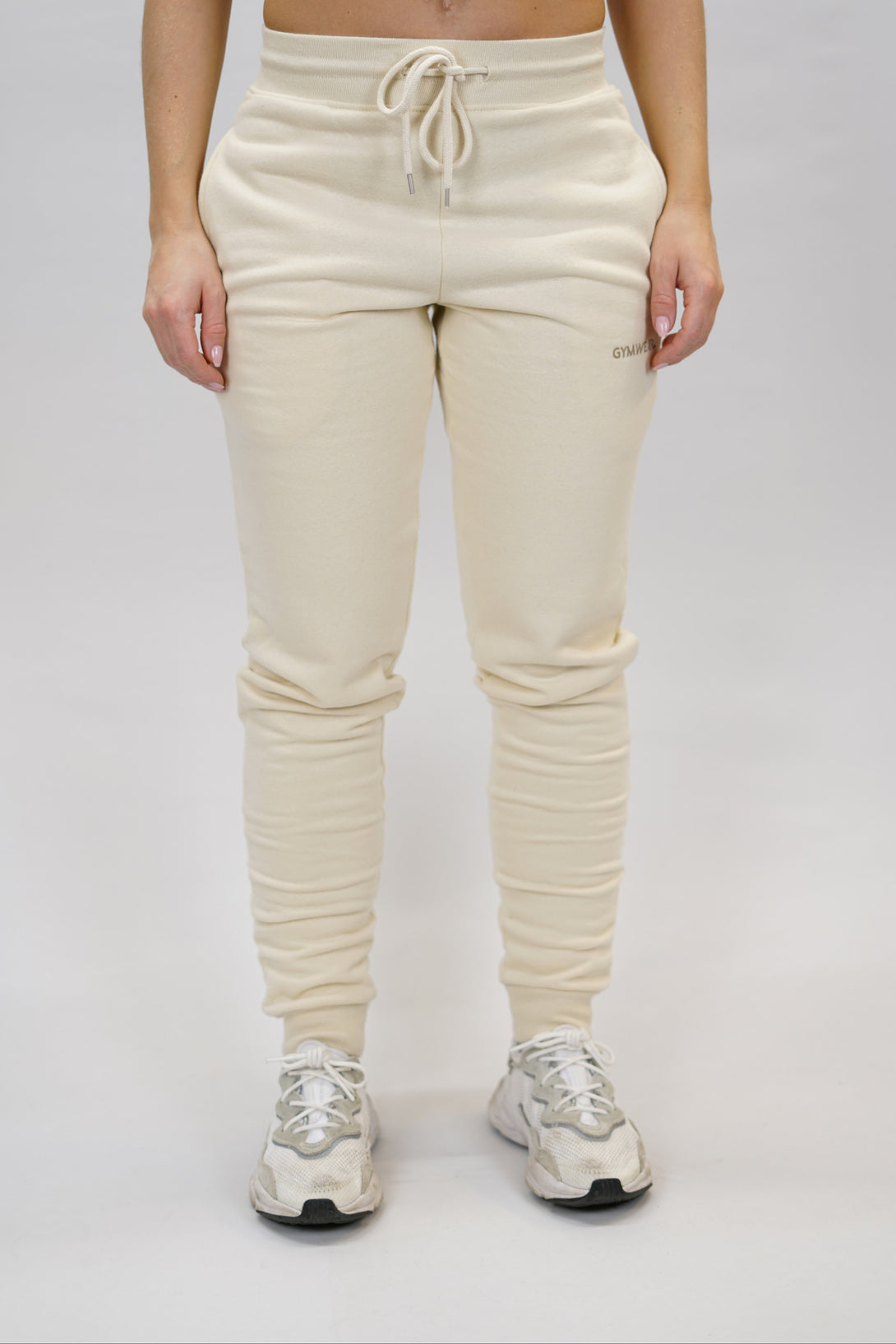 Bekväma joggers i premium borstad bomull. JOGGER RAY har elastisk midja med justerbar dragsko, praktiska sidfickor och avsmalnande passform för en modern look. Perfekta för både träning och vardagsbruk. Beige färg med diskret Gymwear-logga på vänster lår.