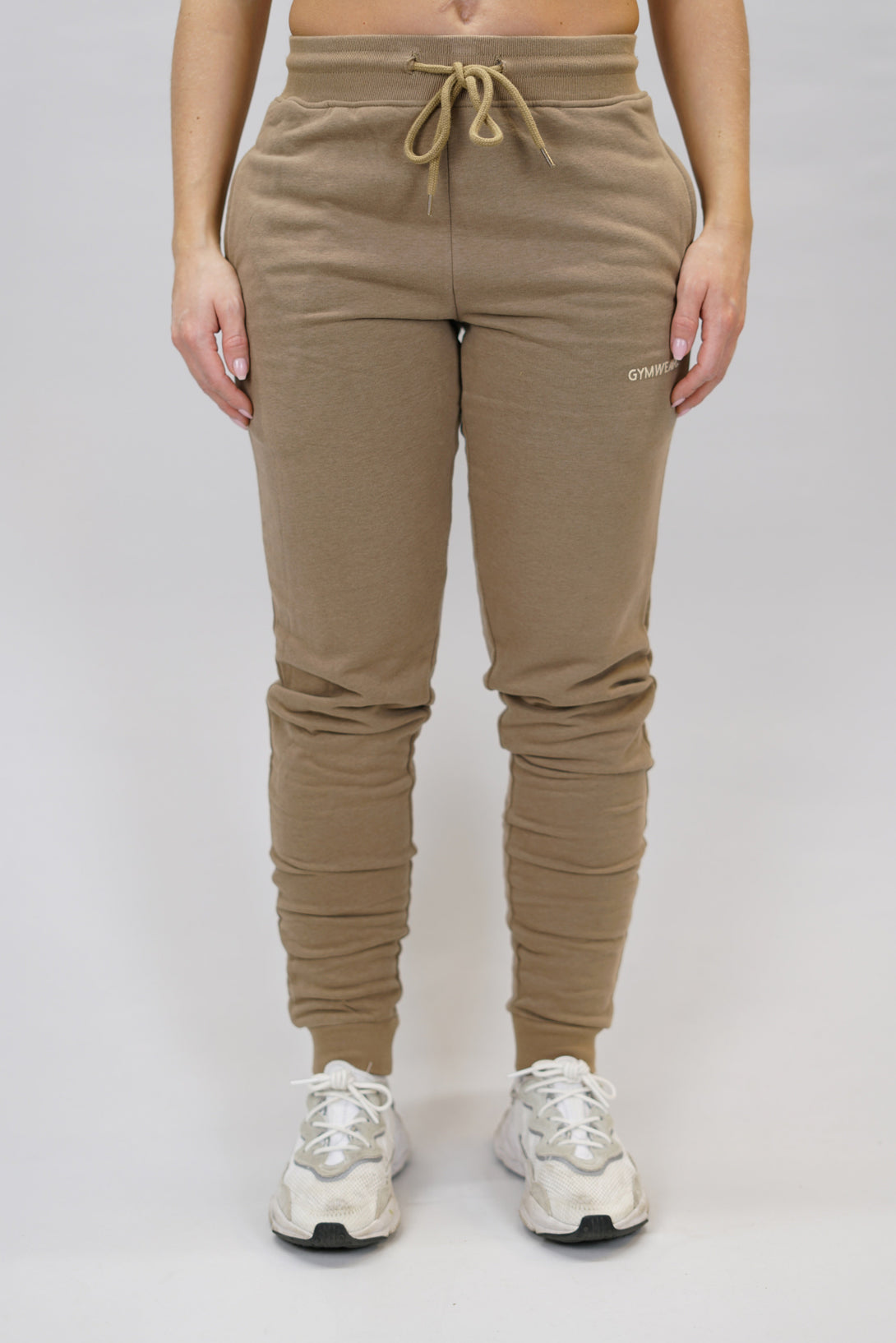 Bekväma joggers i premium borstad bomull. JOGGER RAY har elastisk midja med justerbar dragsko, praktiska sidfickor och avsmalnande passform för en modern look. Perfekta för både träning och vardagsbruk. Brun färg med diskret Gymwear-logga på vänster lår.