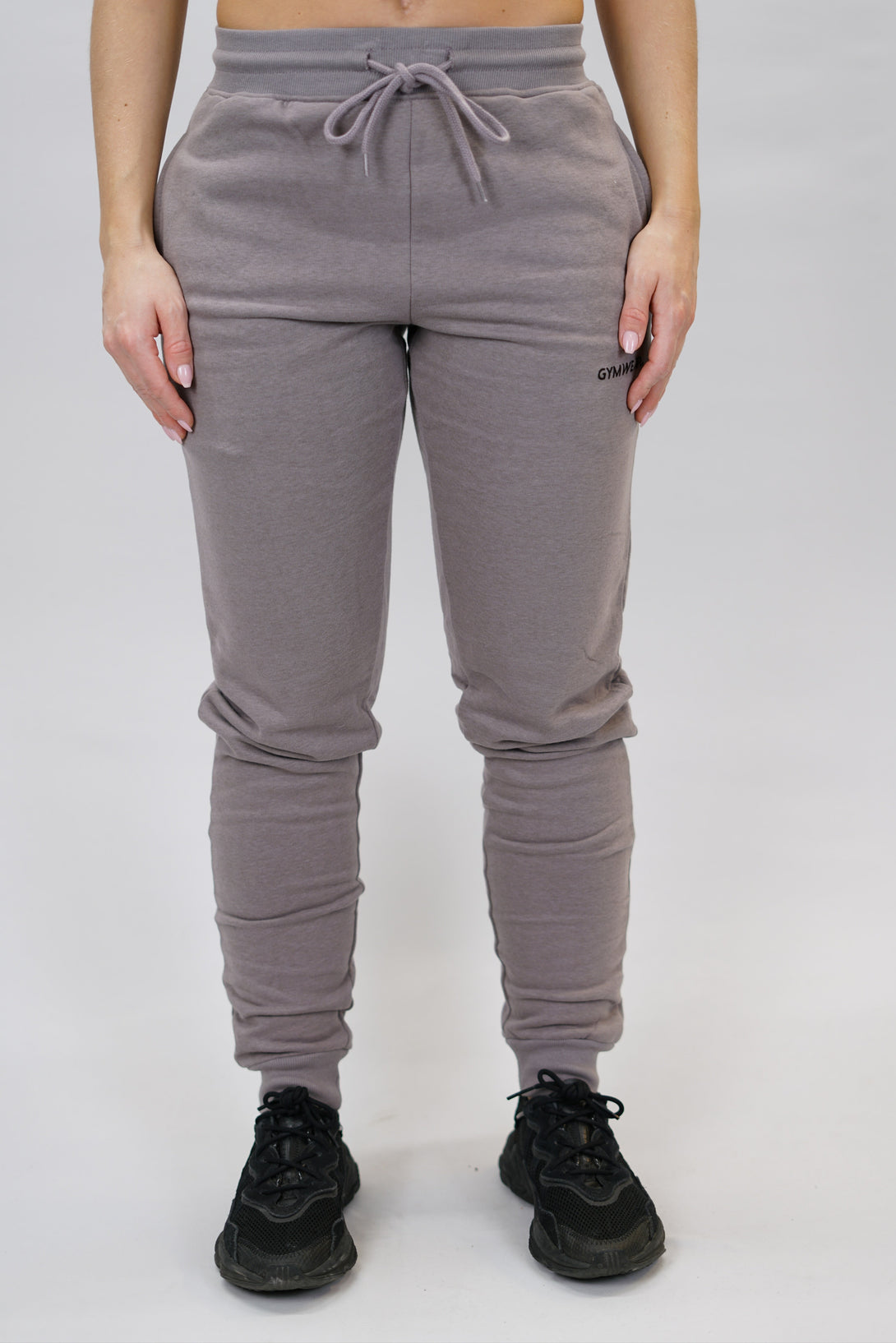 Bekväma joggers i premium borstad bomull. JOGGER RAY har elastisk midja med justerbar dragsko, praktiska sidfickor och avsmalnande passform för en modern look. Perfekta för både träning och vardagsbruk. Zink färg med diskret Gymwear-logga på vänster lår.