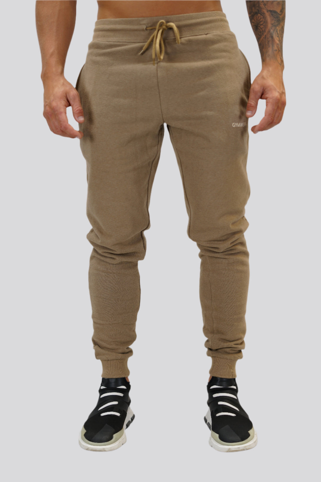 Bekväma JOGGER RAY i premium borstad bomull. Elastisk midja med dragsko, praktiska fickor och avsmalnande passform. Perfekt för träning och vardagsbruk. I färgen brun med Gymwear  logga på vänster lår.